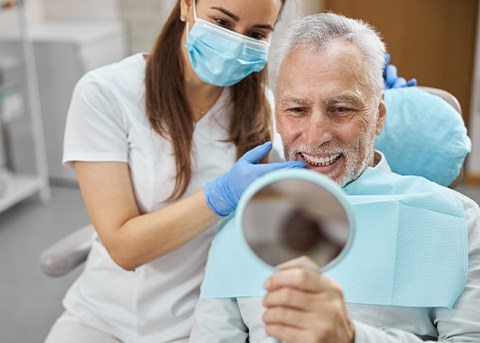 Man in dental chair smiling at mirror with dentist touching his teeth