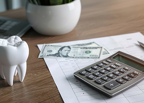 Large model tooth on desk next to calculator, invoice, and dollar bills.