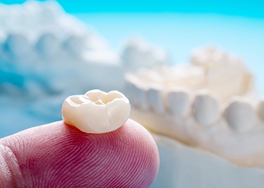 Closeup of dental crown on someone’s fingertip