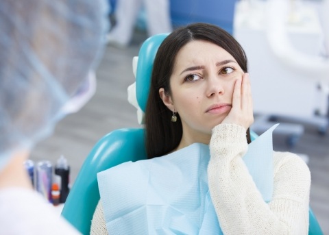 Woman holding her cheek in pain while talking to her emergency dentist