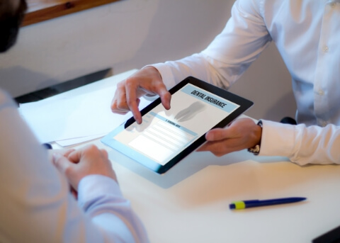 Two people sitting at desk and looking at dental insurance information on tablet