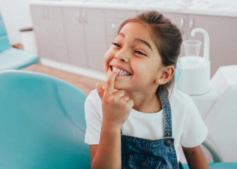 Little girl in dental chair pointing to her smile