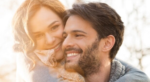 Smiling man and woman hugging outdoors on sunny day