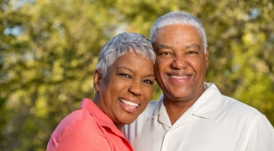 Older man and woman hugging in front of trees