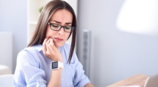 Woman in glasses wincing and holding her jaw in pain
