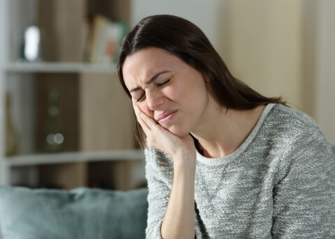 Woman siting on couch and holding her cheek in pain