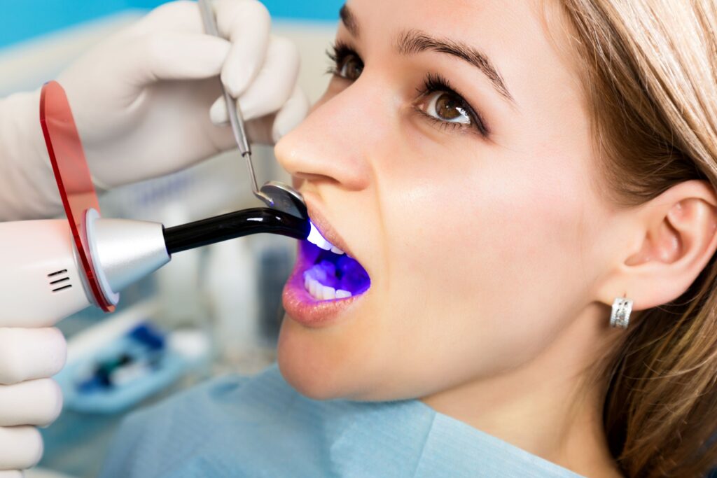 Woman looking at dentist holding UV light to harden filling on her tooth