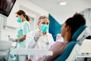Dentist working with patient with hygienist in background.
