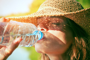 Woman with straw hat drinking from a bottle of water